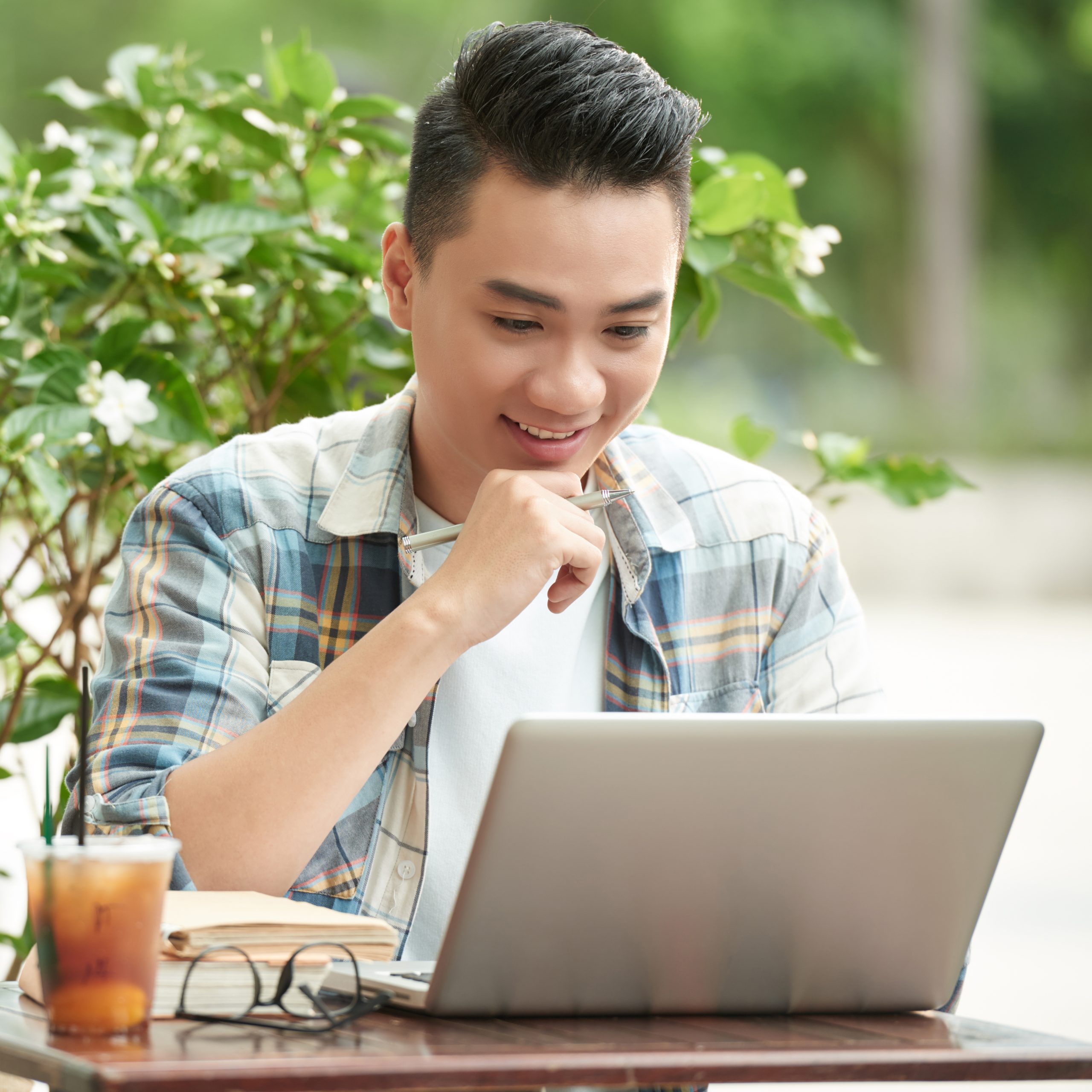 Smiling Vietnamese man working on laptop in outdoor cafe