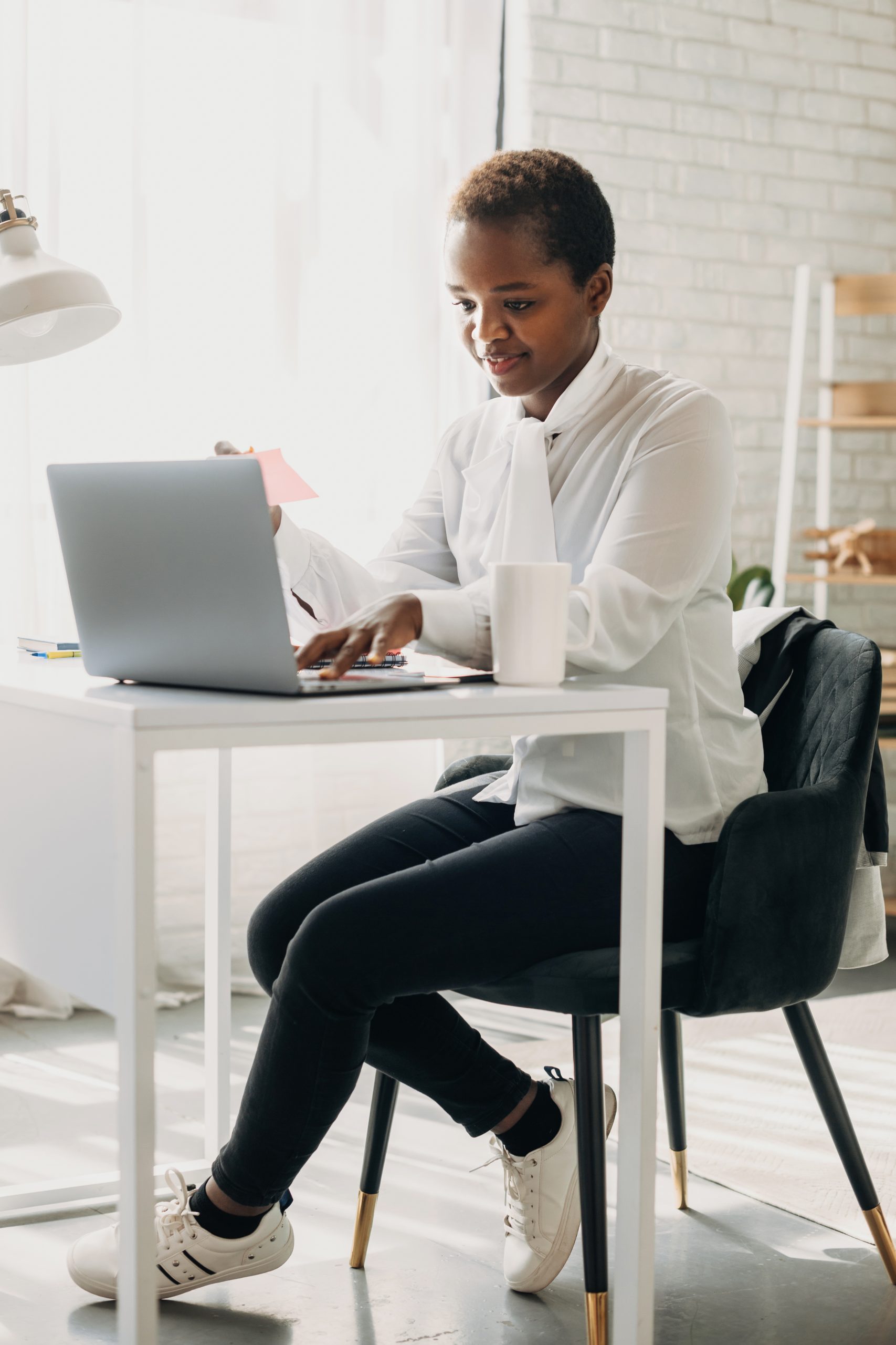 Side view of an african woman secretary typing on a laptop while sitting at the table in a modern office. Beautiful black woman. Future technology. Side view of an african woman secretary typing on a laptop while sitting at the table in a modern office. Beautiful black woman. Future technology.