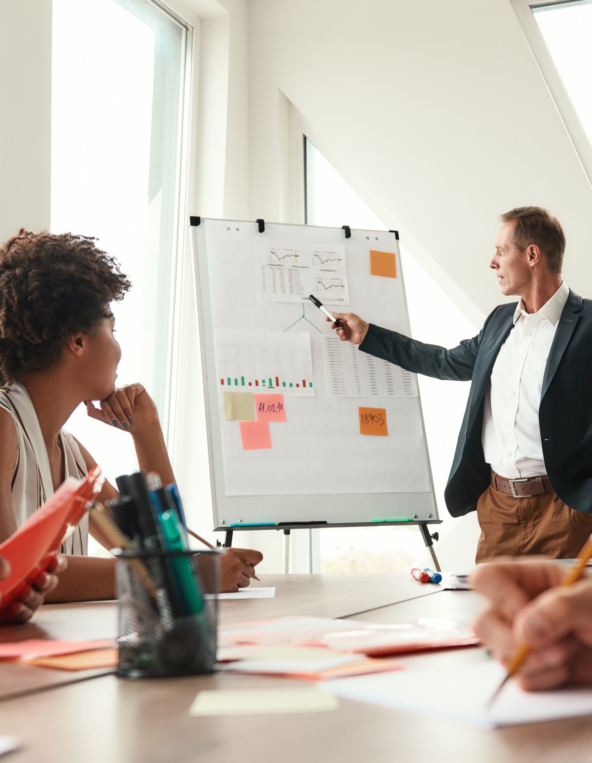 Discussing new project. Mature businessman standing near whiteboard and explaining something to his colleagues Discussing new project. Mature businessman standing near whiteboard and explaining something to his colleagues. Teamwork. Meeting