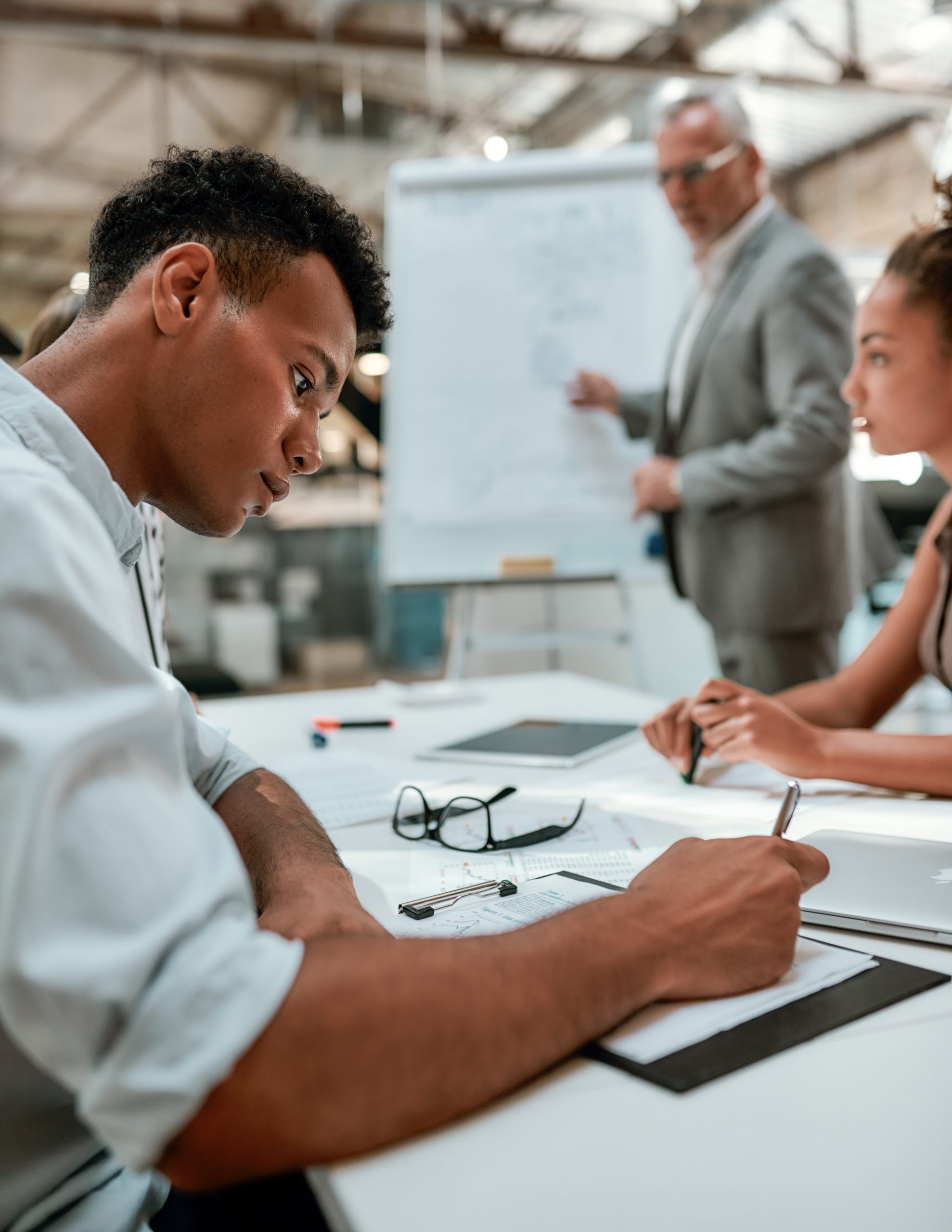 Important information. Young afro american man is writing something while his colleague explaining new business strategy with white board on the background. Meeting. Teamwork