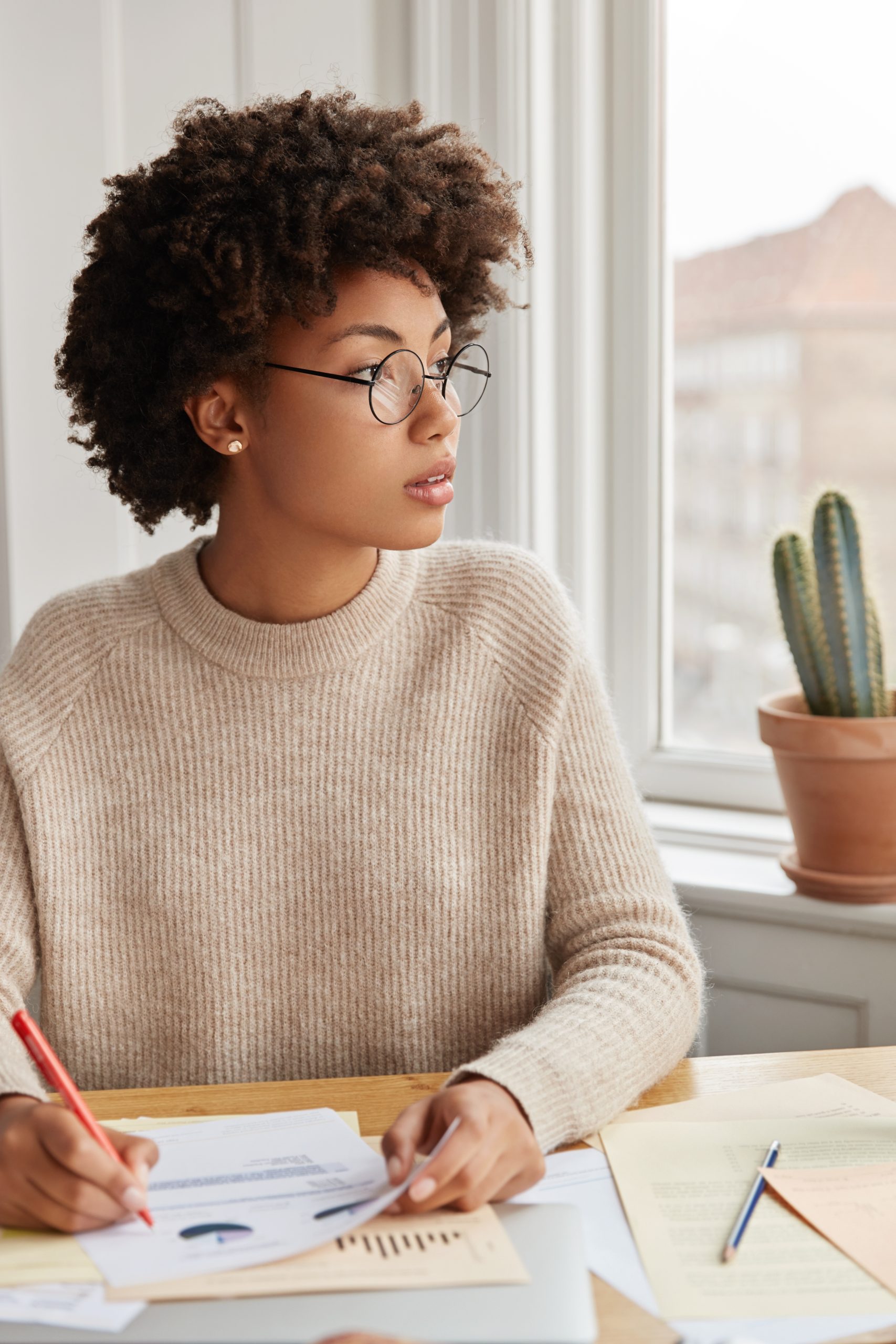 Pensive black businesswoman makes notes in documents, sits at desktop at modern apartment, dressed in casual loose sweater. Busy student writes down homeworks, prepares for tomorrows seminar Pensive black businesswoman makes notes in documents, sits at desktop at modern apartment, dressed in casual loose sweater. Busy student writes down homeworks, prepares for tomorrows seminar