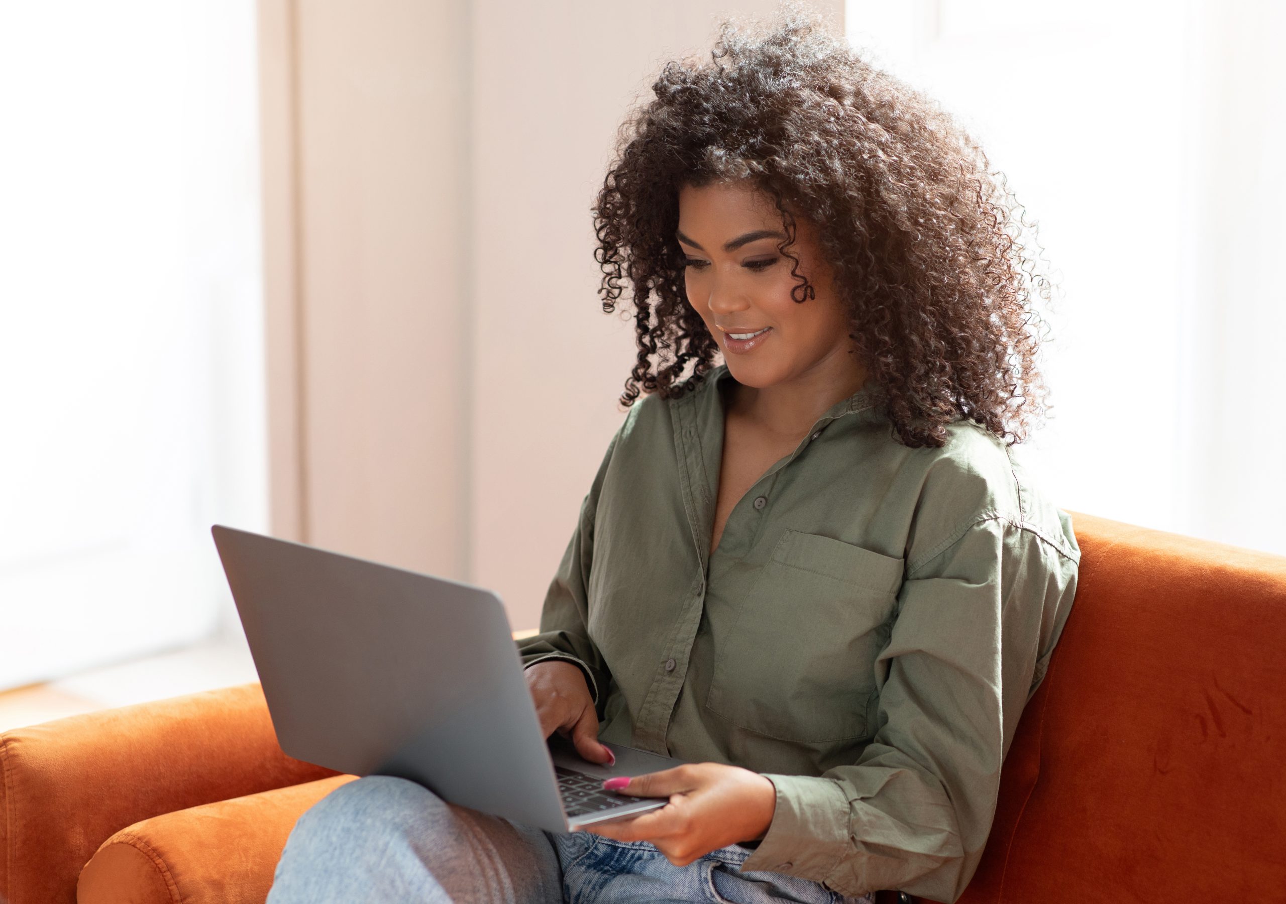 Smiling Black Bushy Woman Working On Laptop Computer A Home Smiling Black Bushy Woman Working On Laptop Computer A Home. Cheerful Freelancer Young Lady Sitting On Couch Using Pc Websurfing And Looking At Screen, Enjoying Remote Online Job